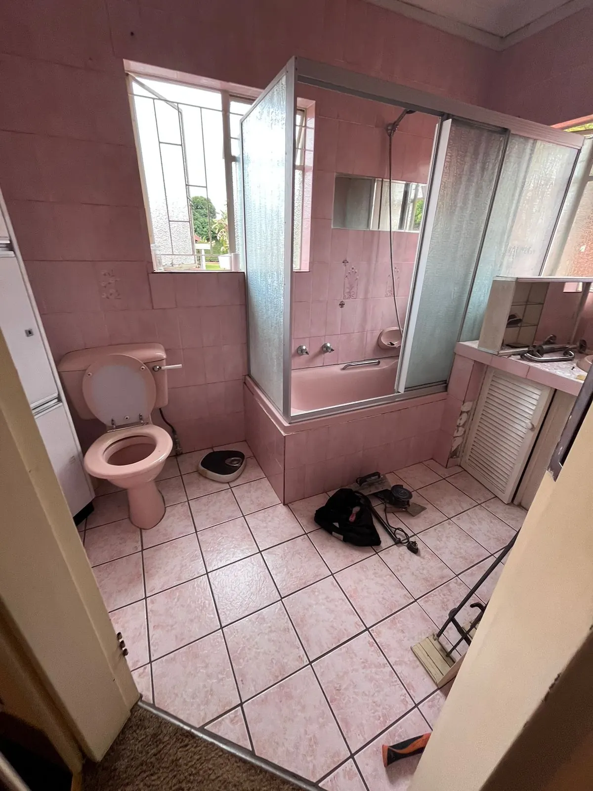 Before: dated pink-tiled bathroom with a bath and sliding shower screen