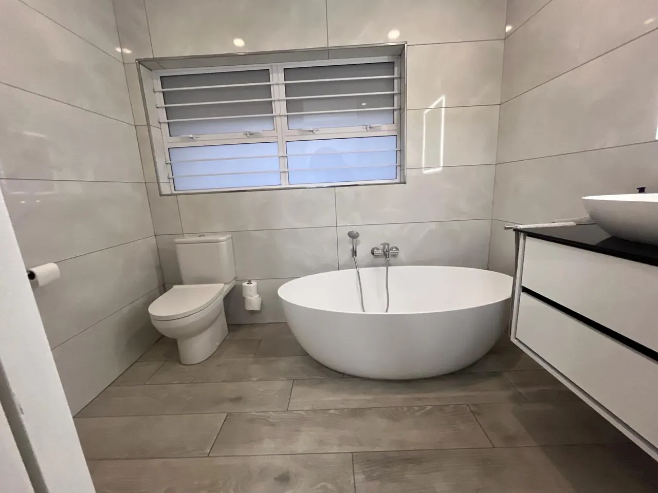After: bathroom with freestanding bath, large-format wall tiles and wood-look floor tiles