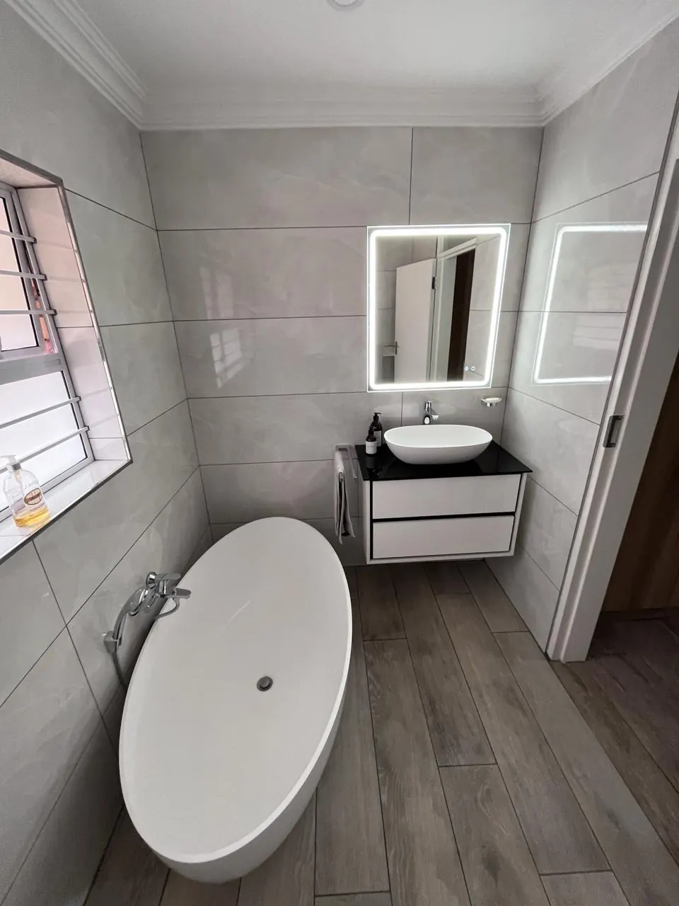 After: floating vanity with vessel basin, black glass top and LED mirror beside a freestanding bath