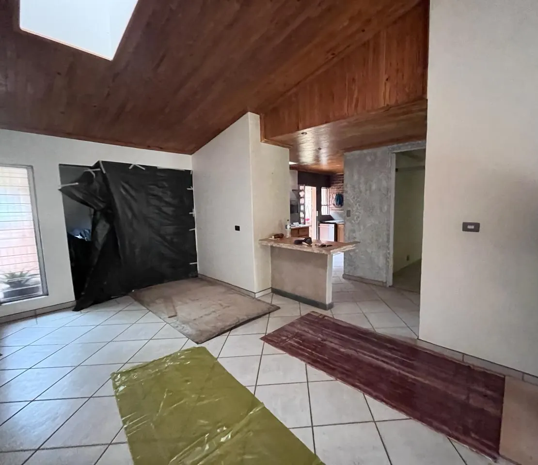 Before: open-plan living area with a dark timber ceiling and an old breakfast counter, during the strip-out