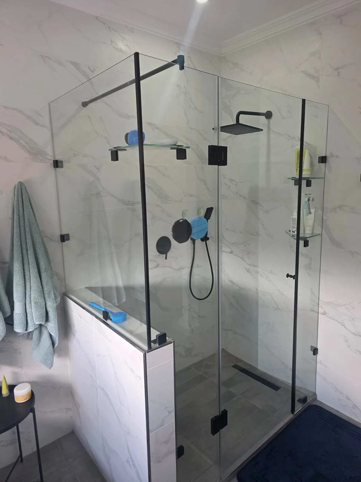 Walk-in shower with frameless glass enclosure, black rain head and mixer, glass shelves and linear floor drain
