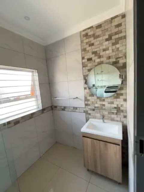 After: bathroom with brick-look mosaic feature wall, round mirror, timber vanity and large-format wall tiles