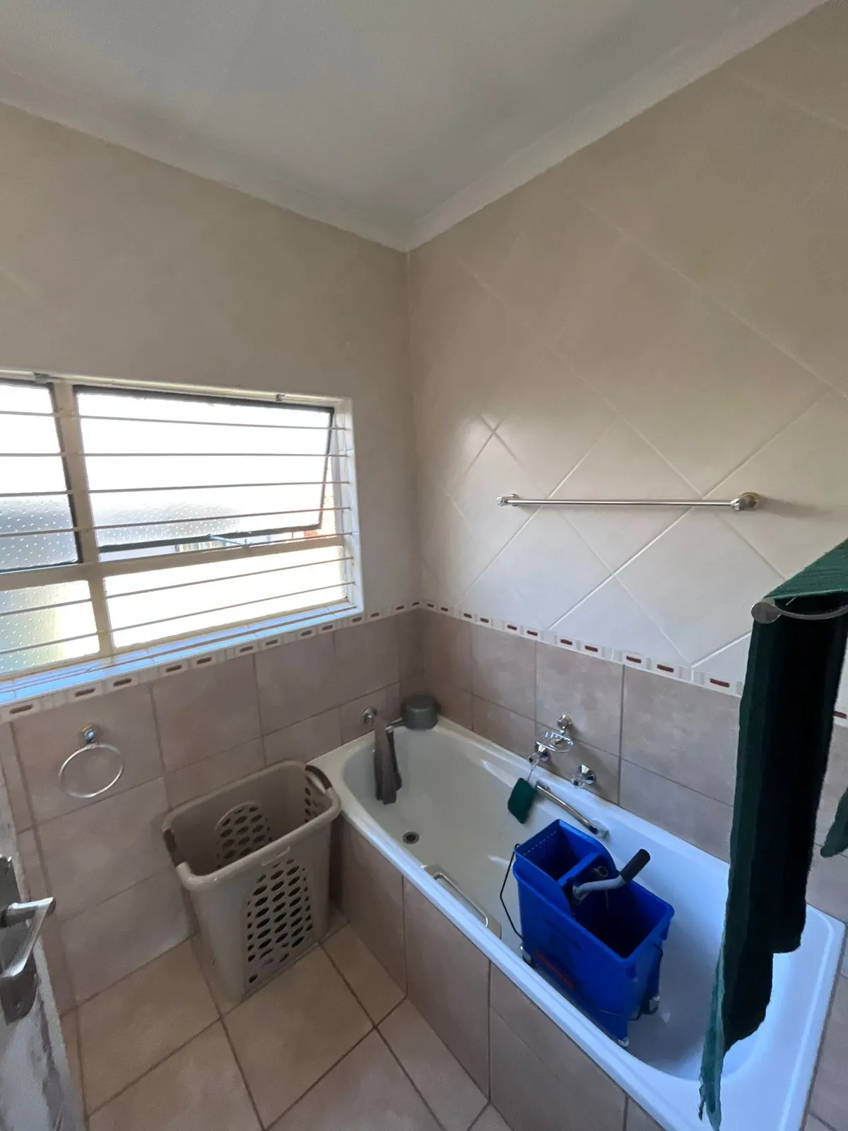 Before: dated bathroom with beige diagonal wall tiles, a border strip and a tiled-in bath