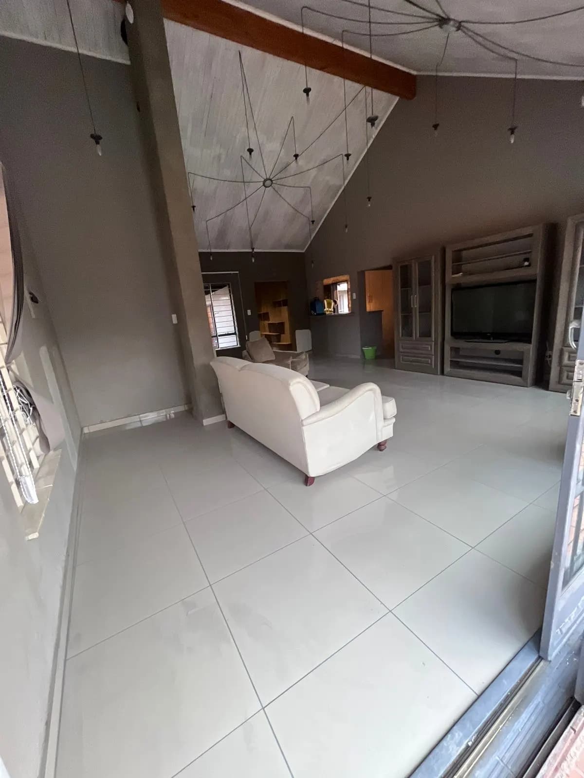 After: open-plan living area with new large-format white porcelain floor tiles under a vaulted ceiling