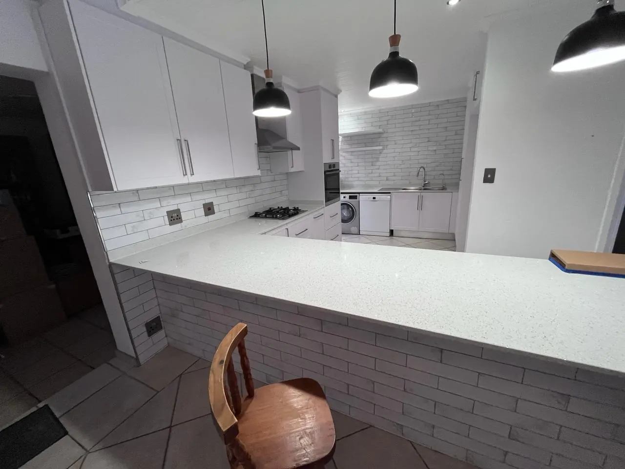 After: white shaker kitchen with a speckled white breakfast counter, brick-look tiles and black pendant lights