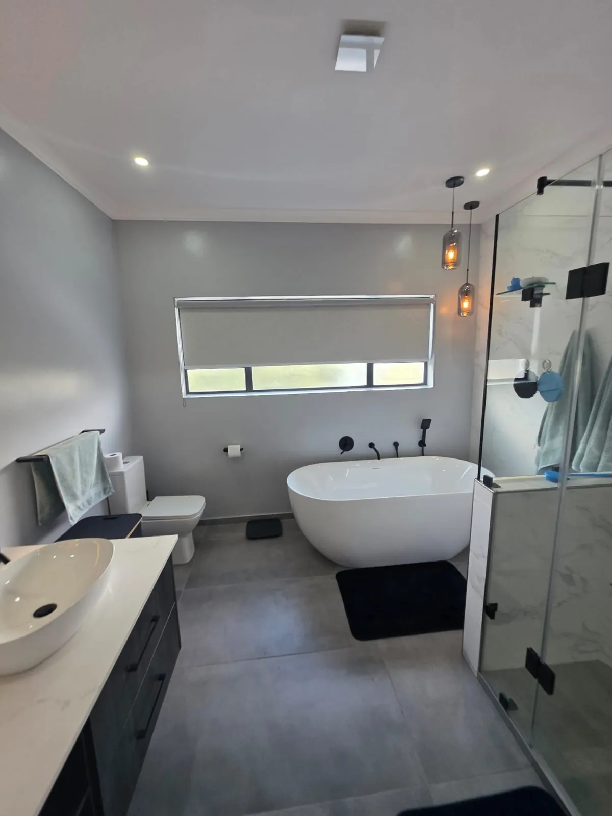 Main bathroom with freestanding bath, wall-mounted black bath mixer and hand shower, pendant lights and large-format grey floor tiles
