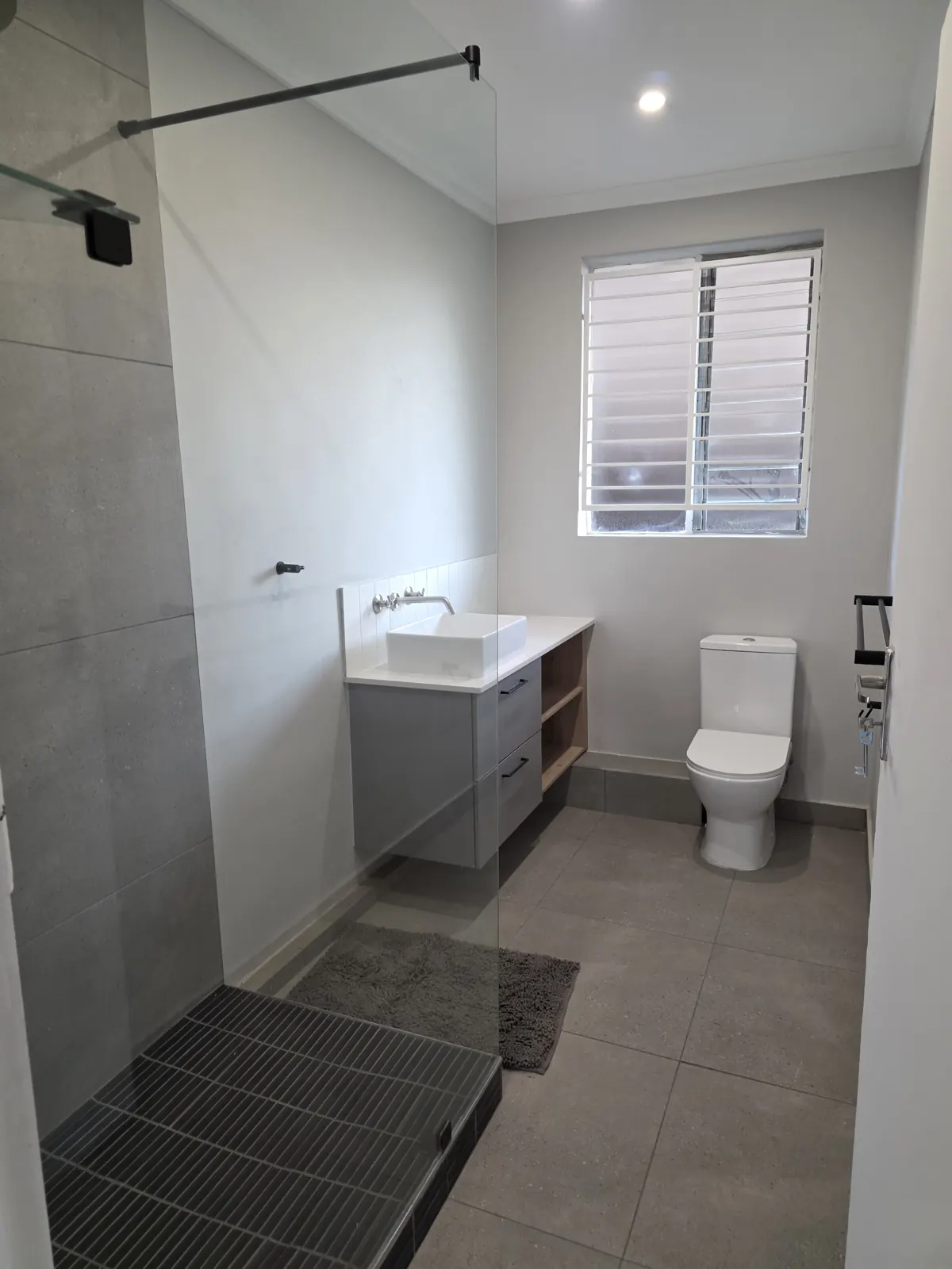 After: bathroom with frameless walk-in shower, black-tiled shower base, floating vanity with vessel basin and wall-mounted mixer