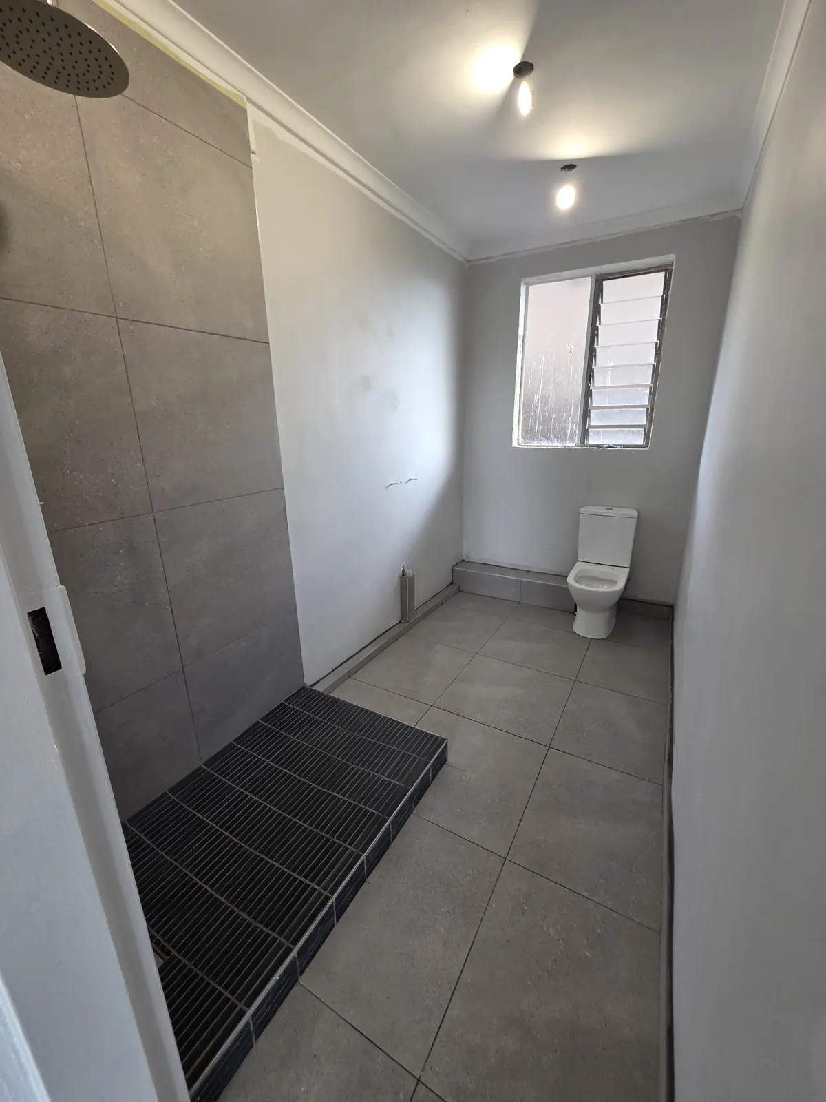 During: new large-format floor and shower wall tiles laid, toilet fitted and shower base tiled, before the vanity and glass go in