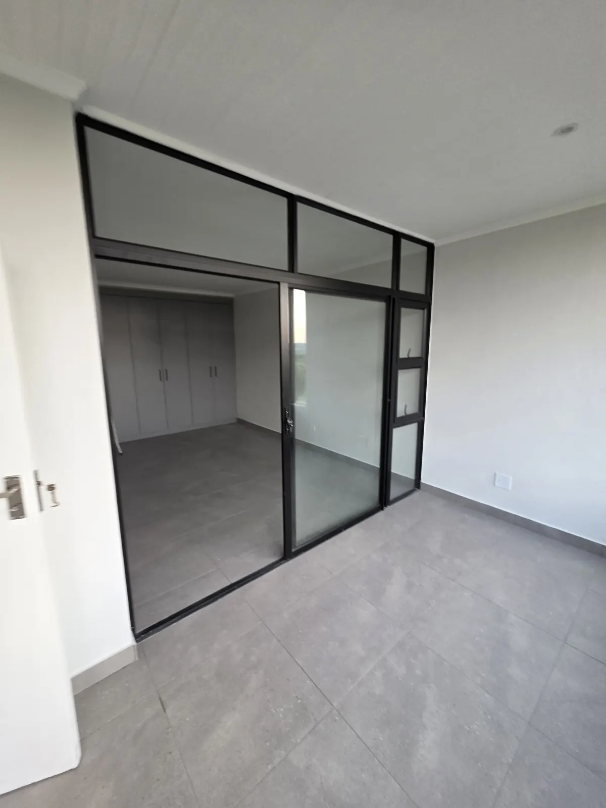After: bedroom seen through the new black-framed glass partition, with built-in cupboards and new grey floor tiles
