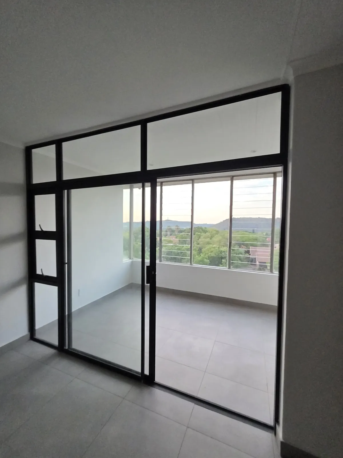 After: new black aluminium glass partition and sliding door, painted ceiling and large grey floor tiles, with views over the trees
