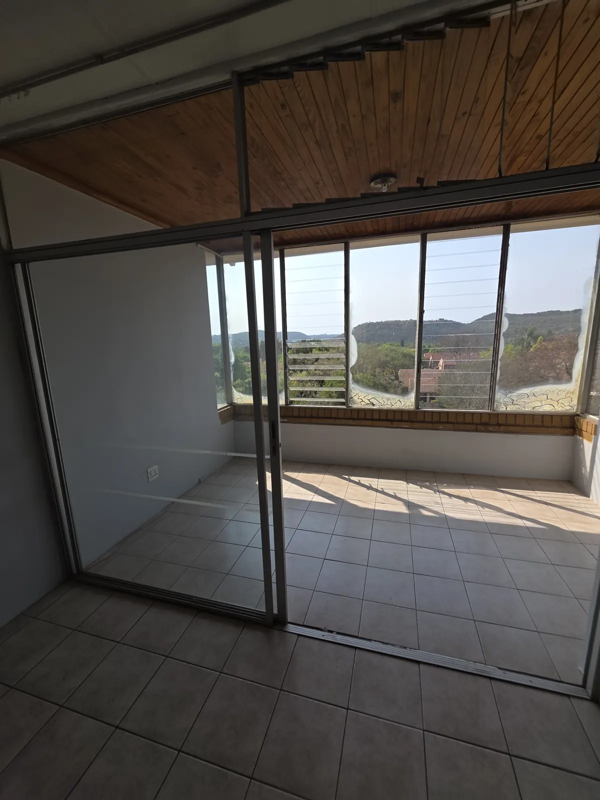 Before: enclosed balcony with a dark knotty pine ceiling, old aluminium sliding door and beige floor tiles