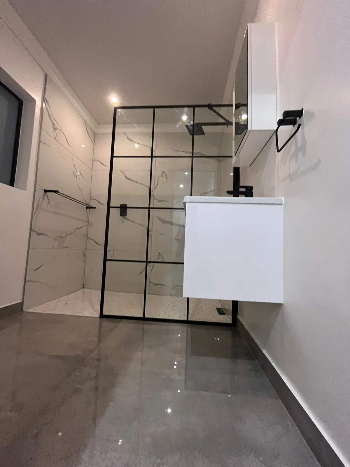 Renovated bathroom with a black grid glass shower screen, floating white vanity and polished grey floor tiles