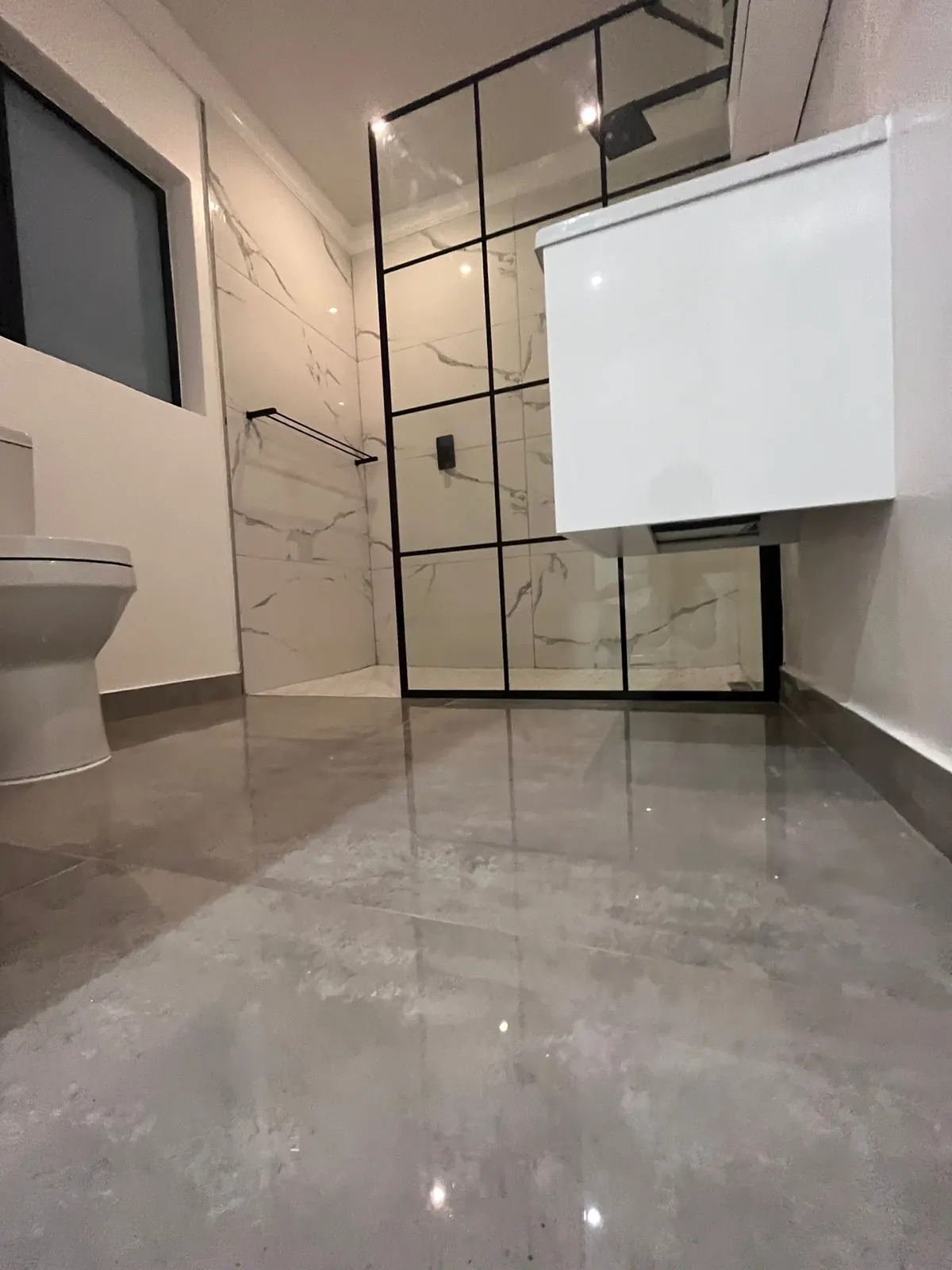 Bathroom with marble-look wall tiles, black grid shower screen and wall-hung white cabinet