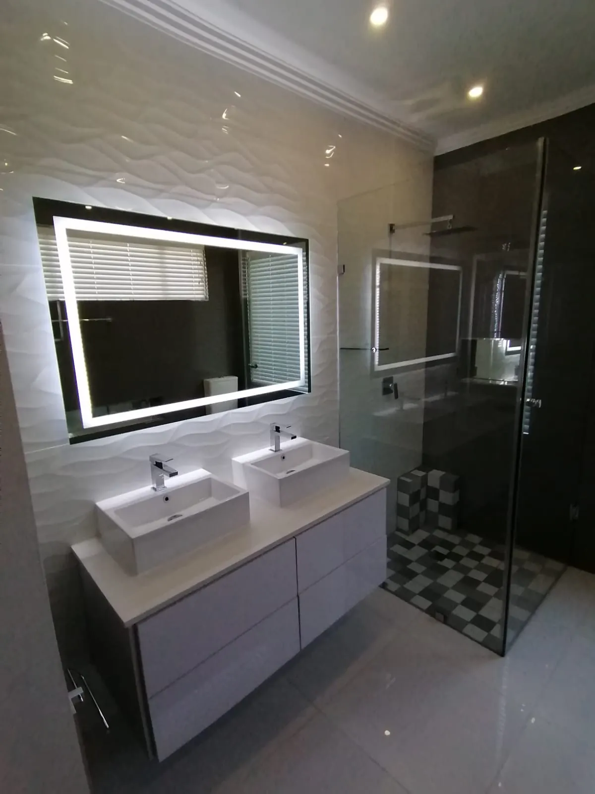 Double-basin vanity with LED mirror beside a walk-in shower