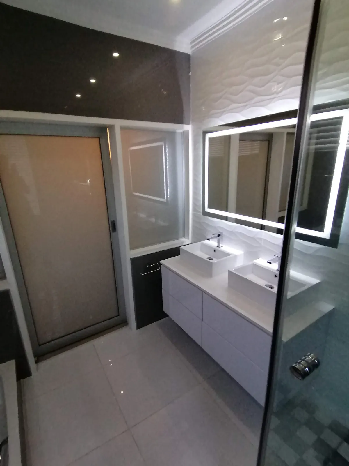 Bathroom with two vessel basins on a white floating vanity, LED mirror and white wave-pattern wall tiles