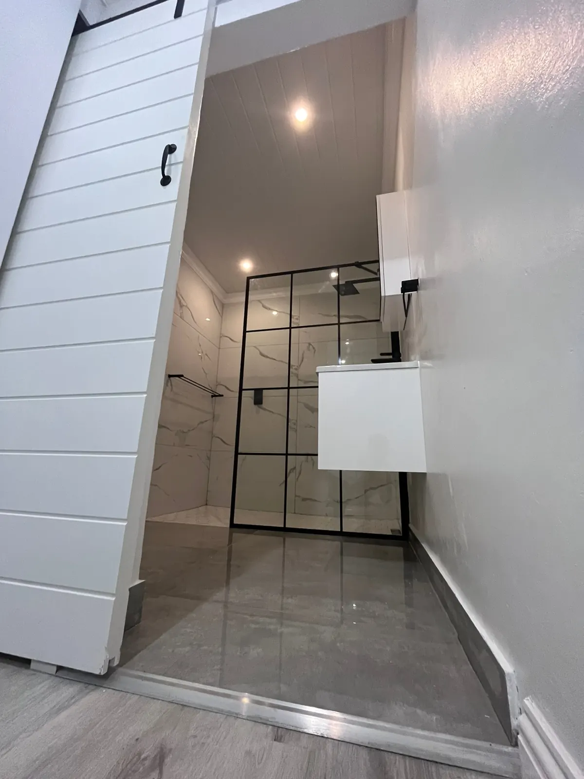 En-suite bathroom behind a white sliding barn door, with a black-framed walk-in shower