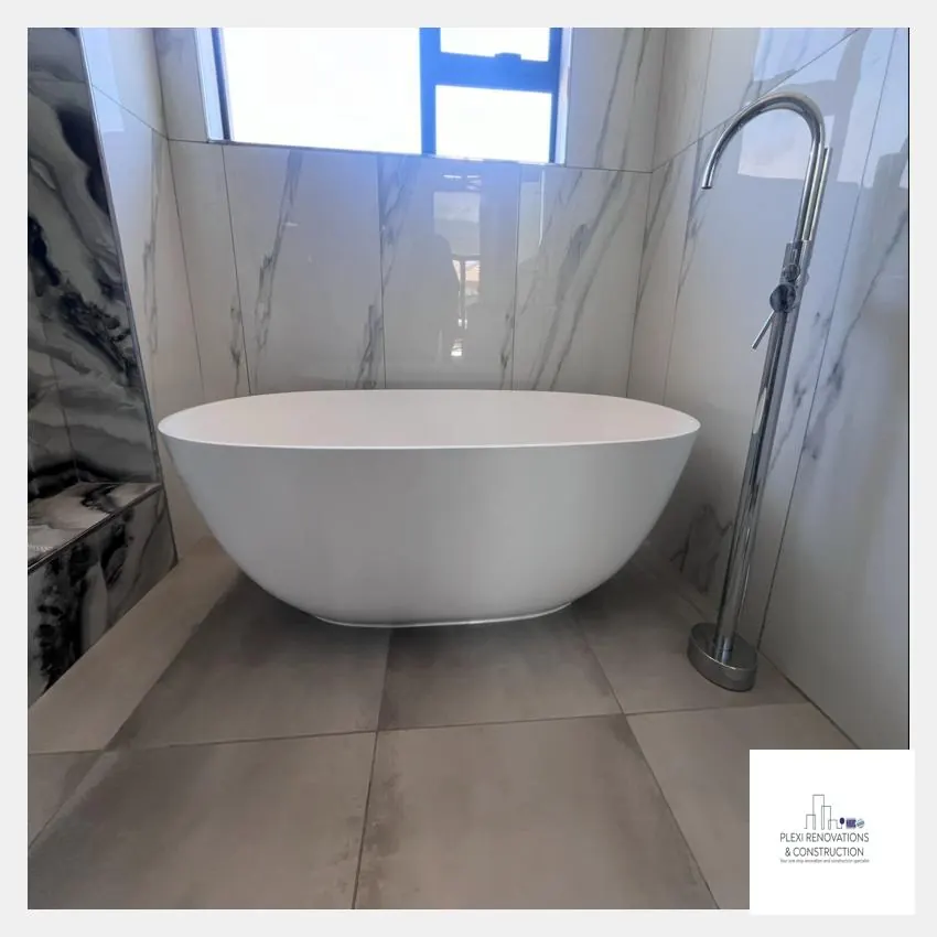 Freestanding white bath with floor-standing mixer against marble-look tiles