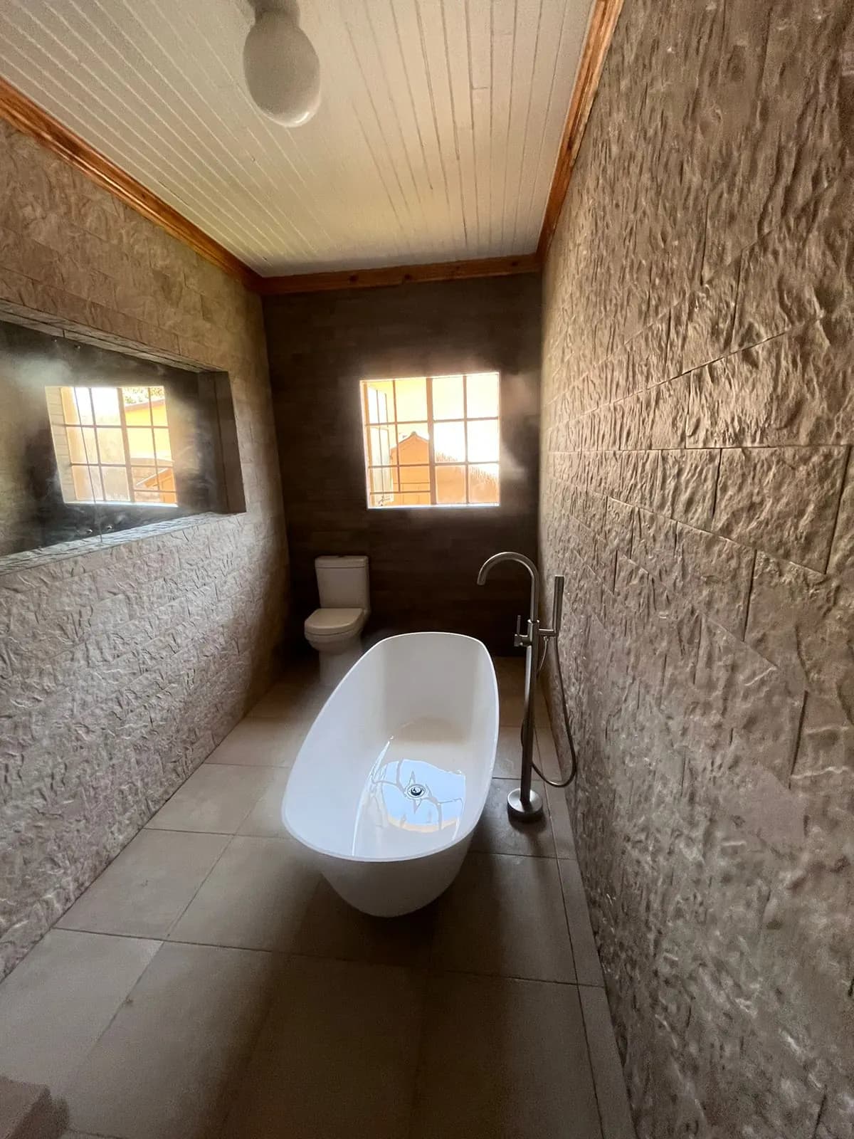 Bathroom with freestanding bath, textured feature wall and timber ceiling