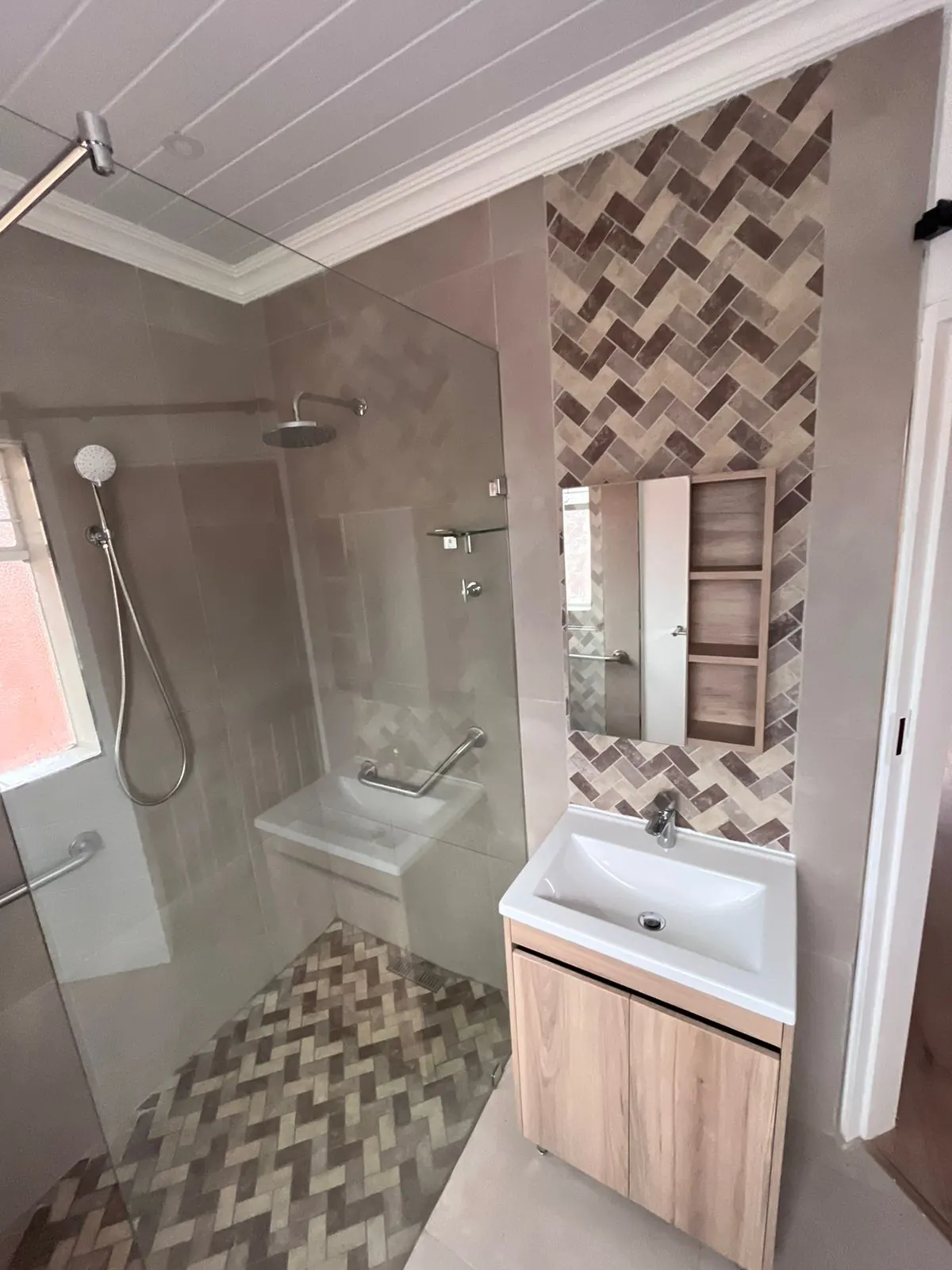 After: walk-in shower with frameless glass, herringbone feature tiles, and a timber vanity with mirror and shelf niche