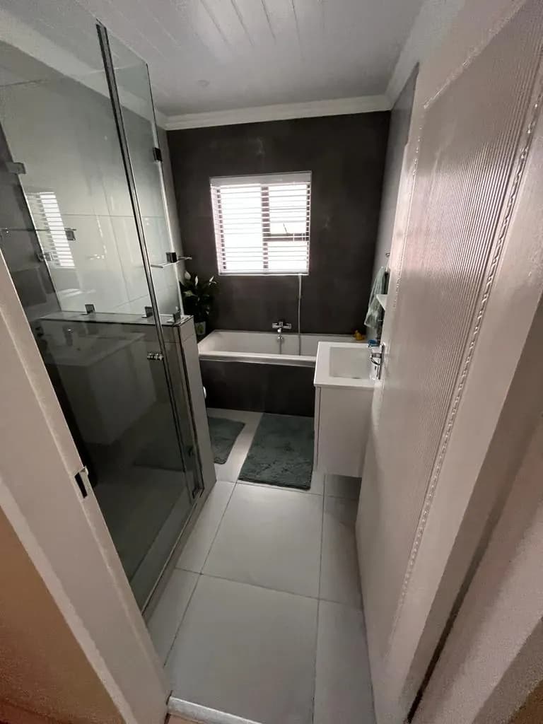 Long bathroom with glass shower in front and bath at the back
