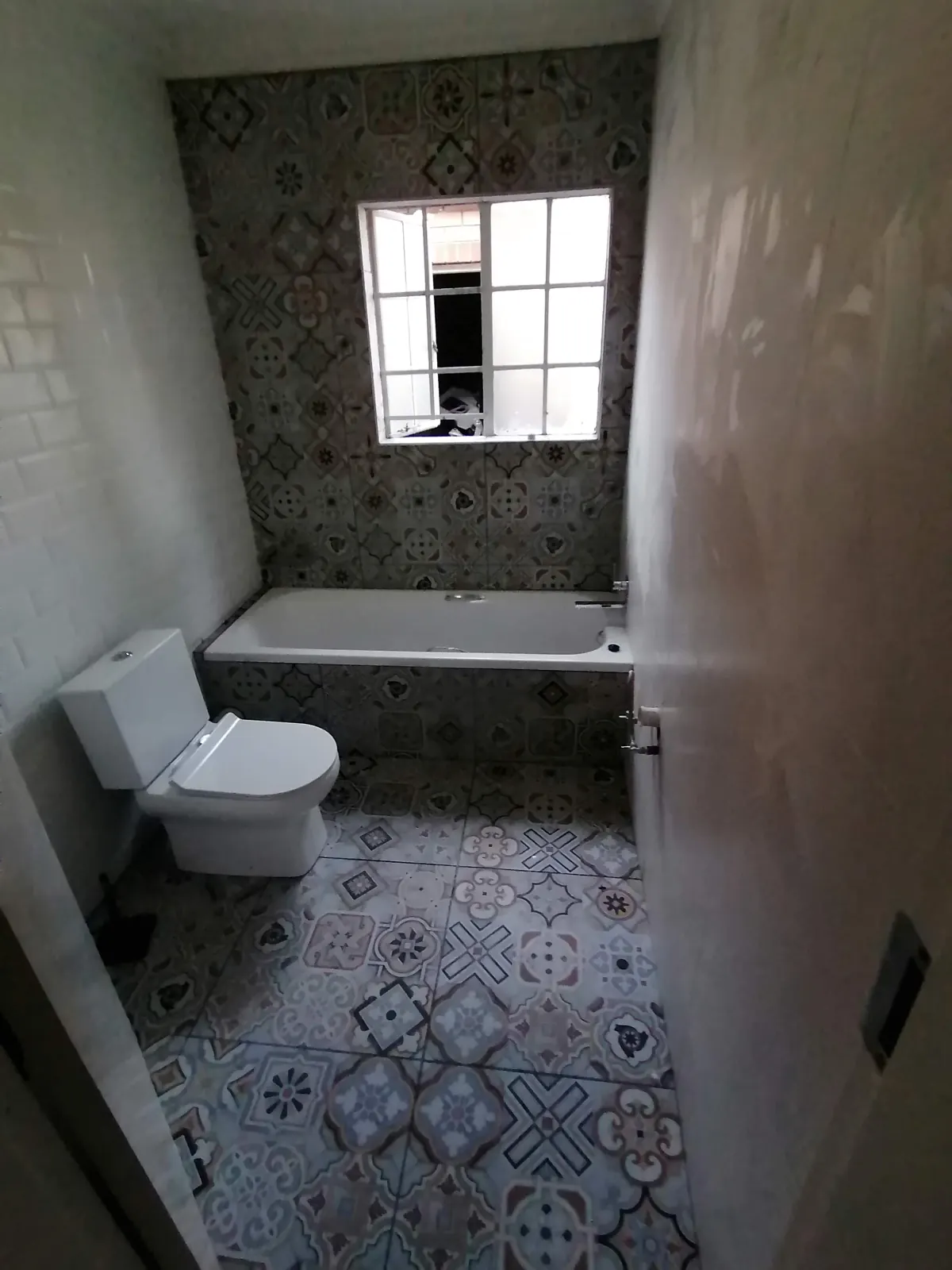 Small bathroom with patterned encaustic-look floor and wall tiles, built-in bath and white subway tiles