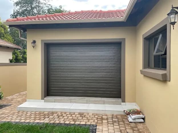 Single garage with dark sectional door, plaster-banded openings and a paved apron
