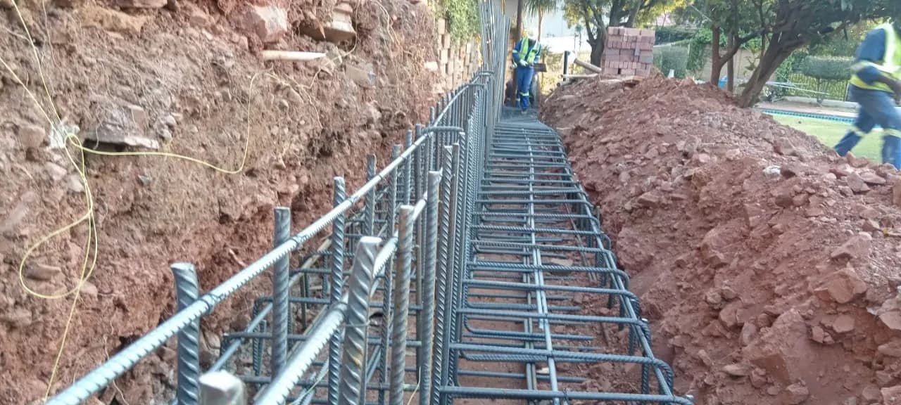 Steel cage for a retaining wall footing in an excavated trench