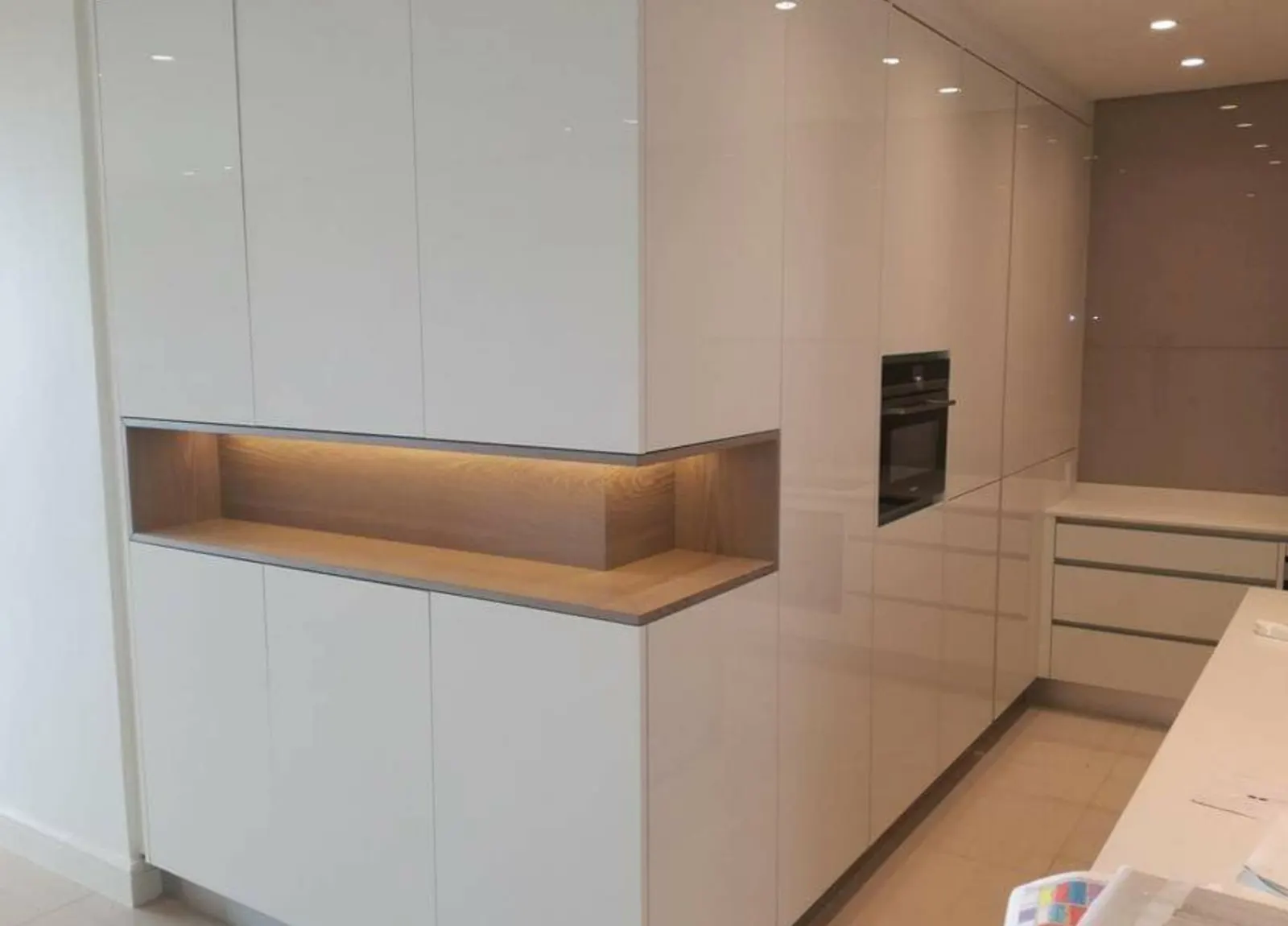 High-gloss white tall kitchen units with a lit timber niche and built-in oven