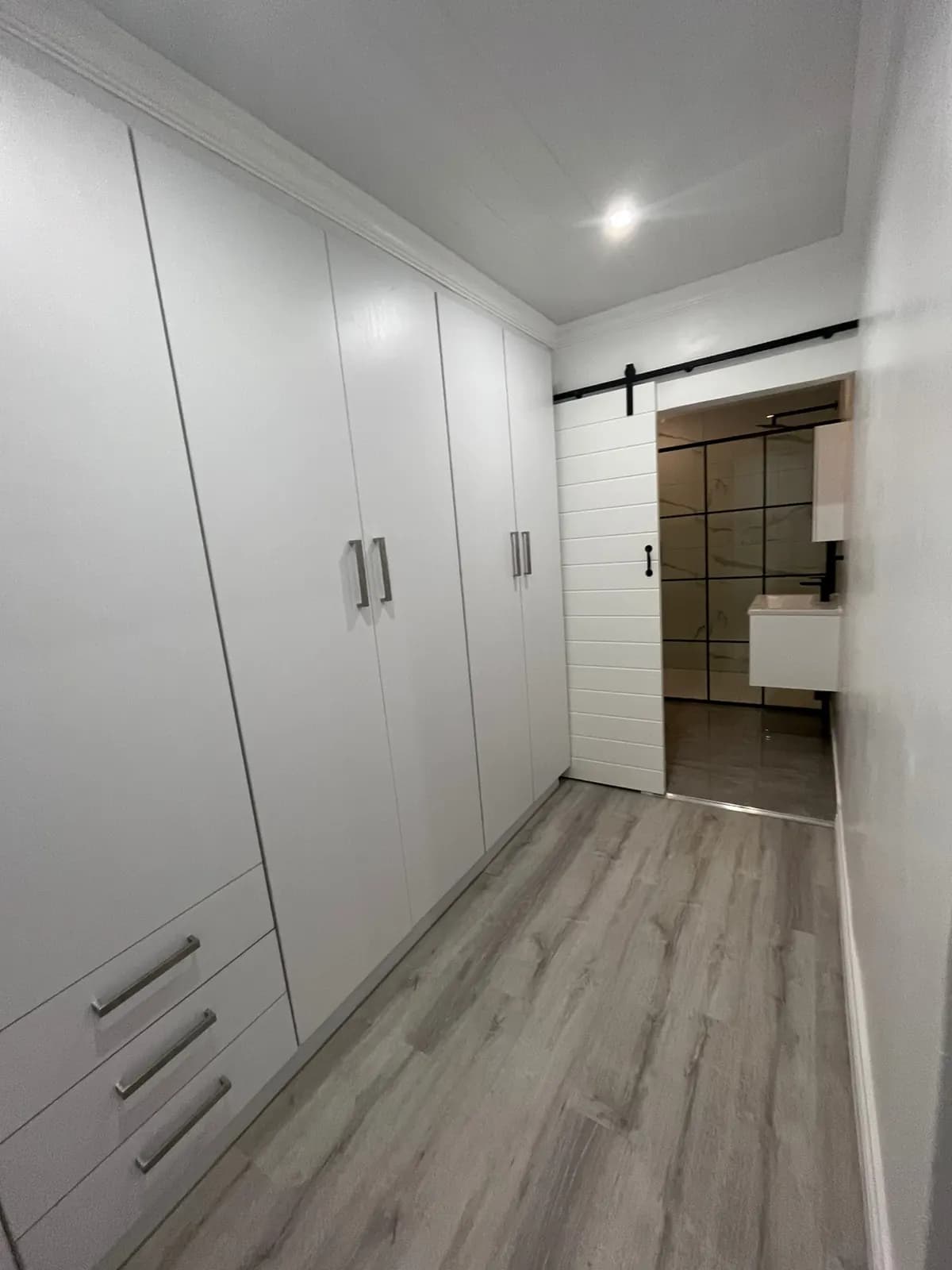 Walk-in wardrobe with white built-in cupboards and barn door to the en-suite