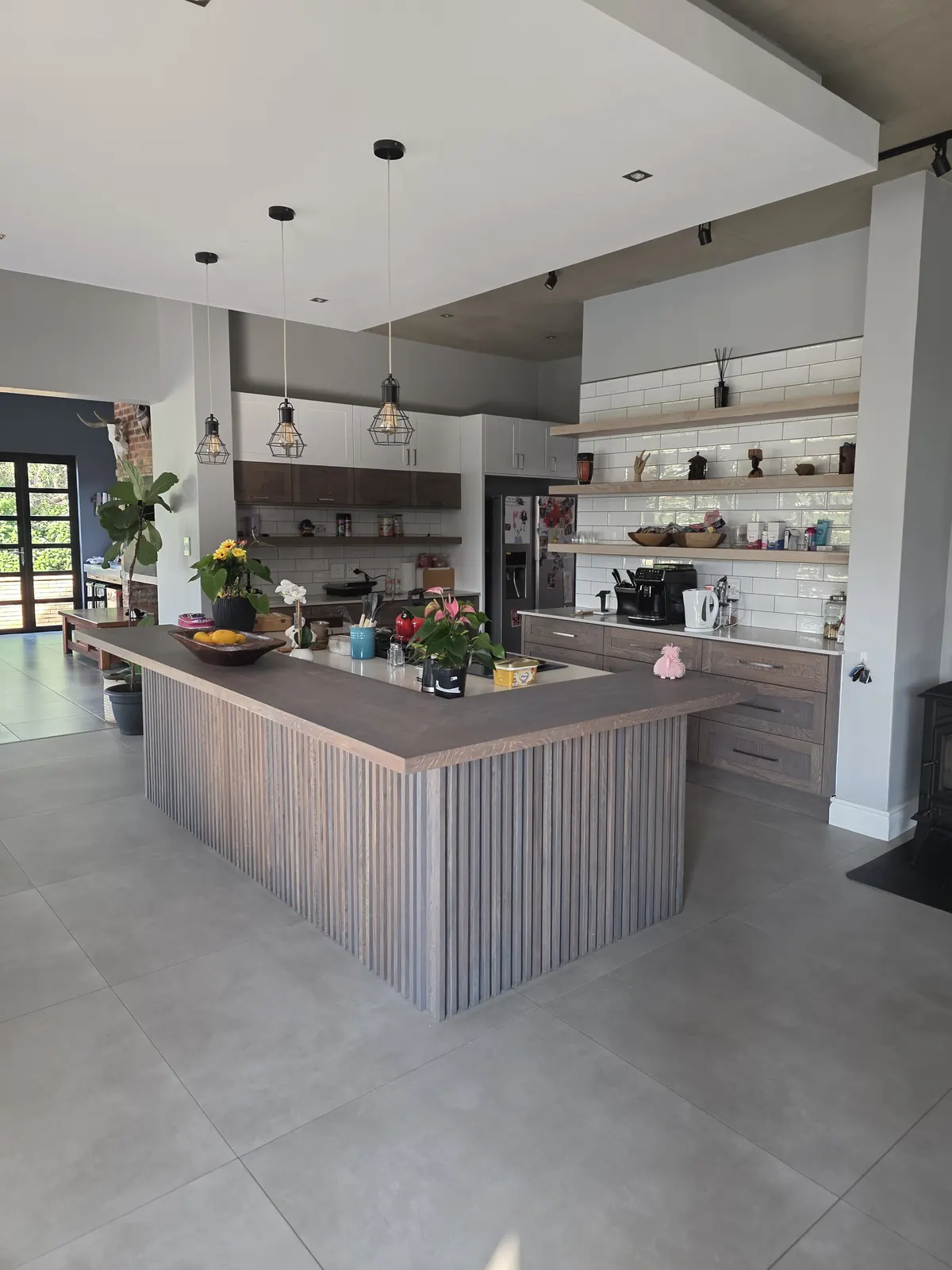Open-plan kitchen with an L-shaped oak slatted island, shaker cupboards and pendant lights