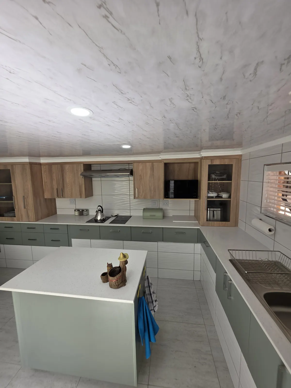 Sage green kitchen with quartz island, double sink and oak glass-front cabinets