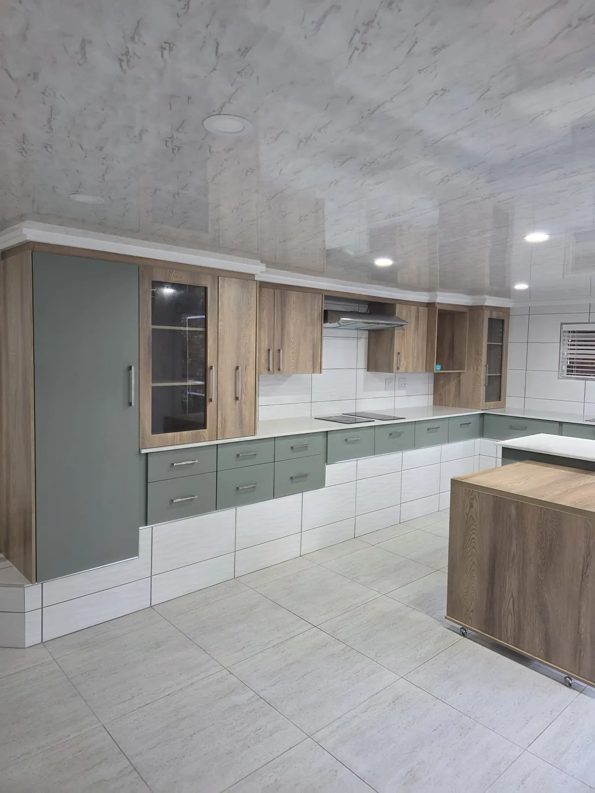 Sage green kitchen drawers and tall pantry with oak wall cabinets and wave-pattern wall tiles
