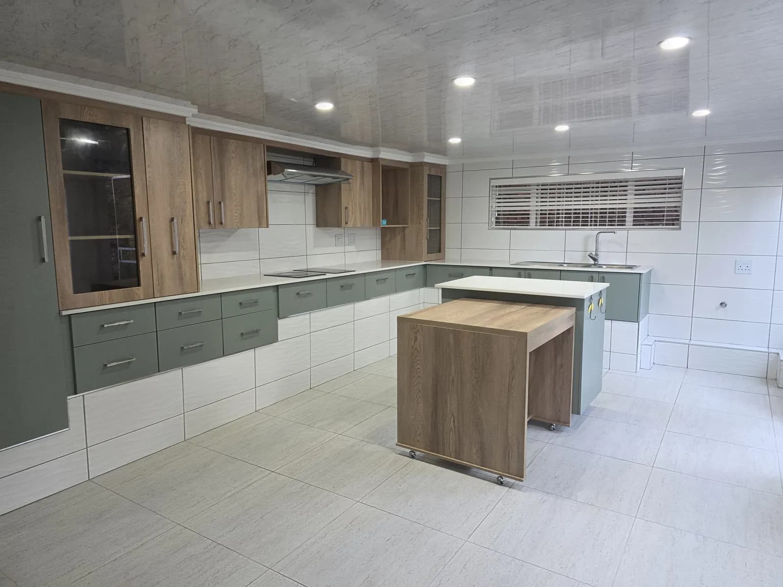 Sage green and oak kitchen with glass-front wall units, white quartz tops and a mobile oak island