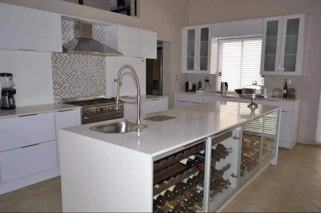 White gloss kitchen with a quartz island holding a glass-fronted wine rack