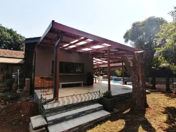 Steel-framed patio pergola with clear roof sheeting over a tiled deck and stone-clad steps