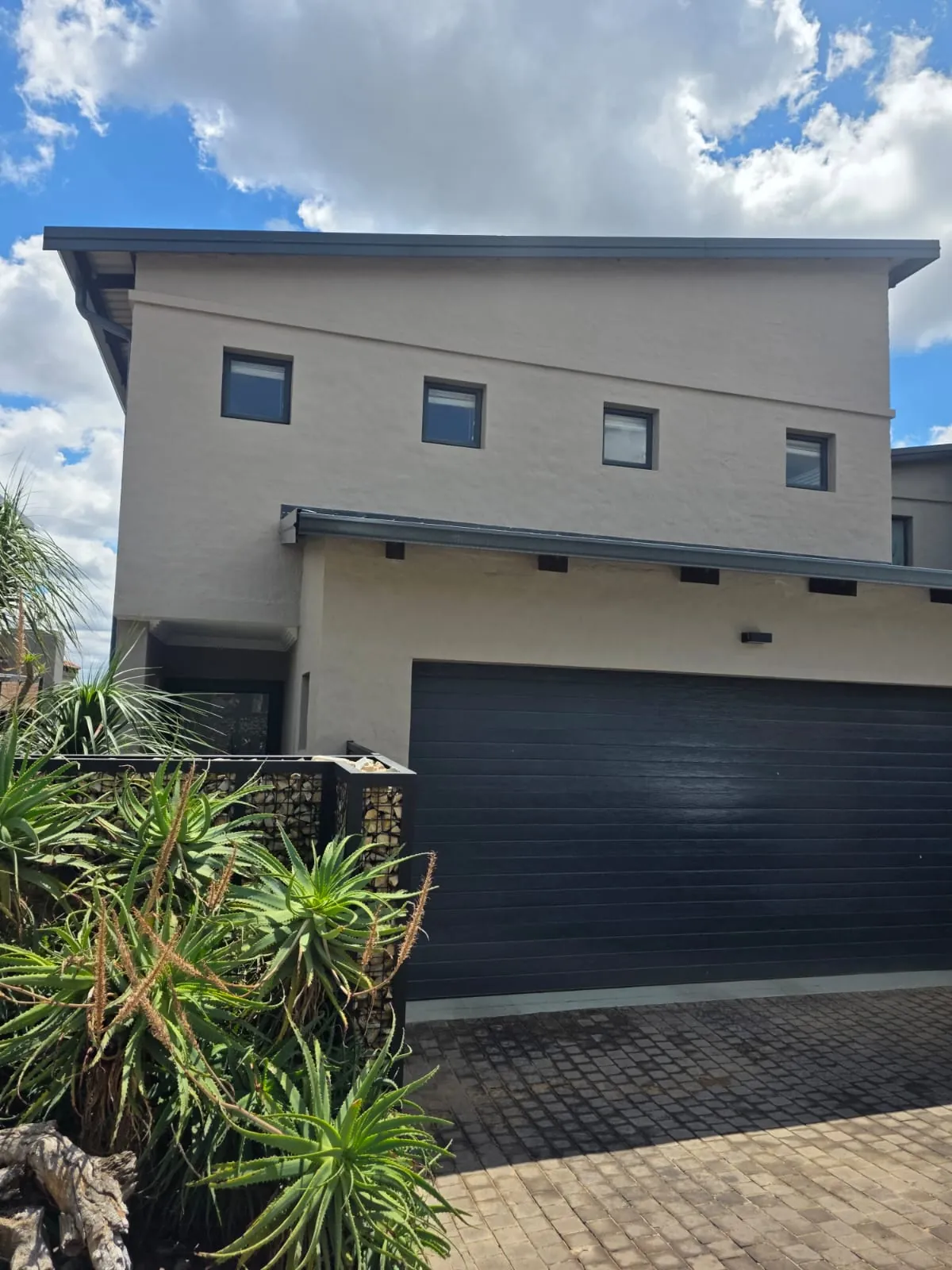 Front of a double-storey home after exterior painting, with gabion wall and aloes