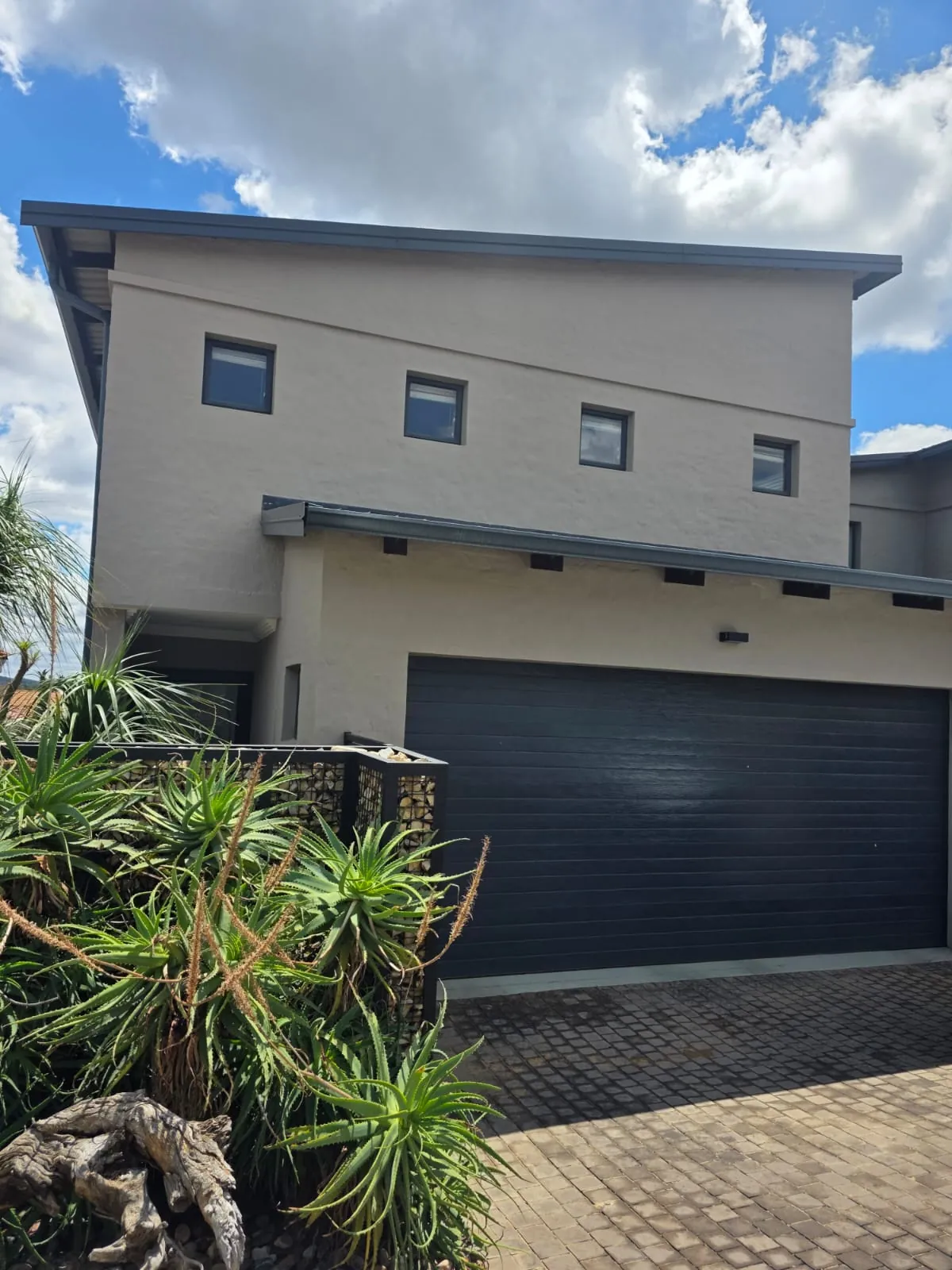Double-storey home repainted outside in warm grey, with dark window frames and a charcoal garage door