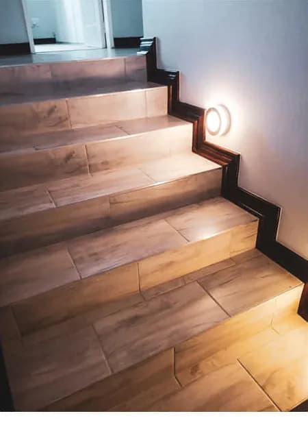 Staircase clad in wood-look porcelain tiles with a dark stepped skirting and wall step light