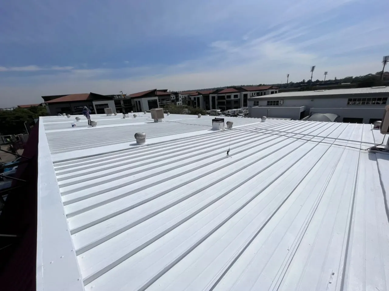 The same commercial roof after a white waterproof coating, with a team member finishing the edge